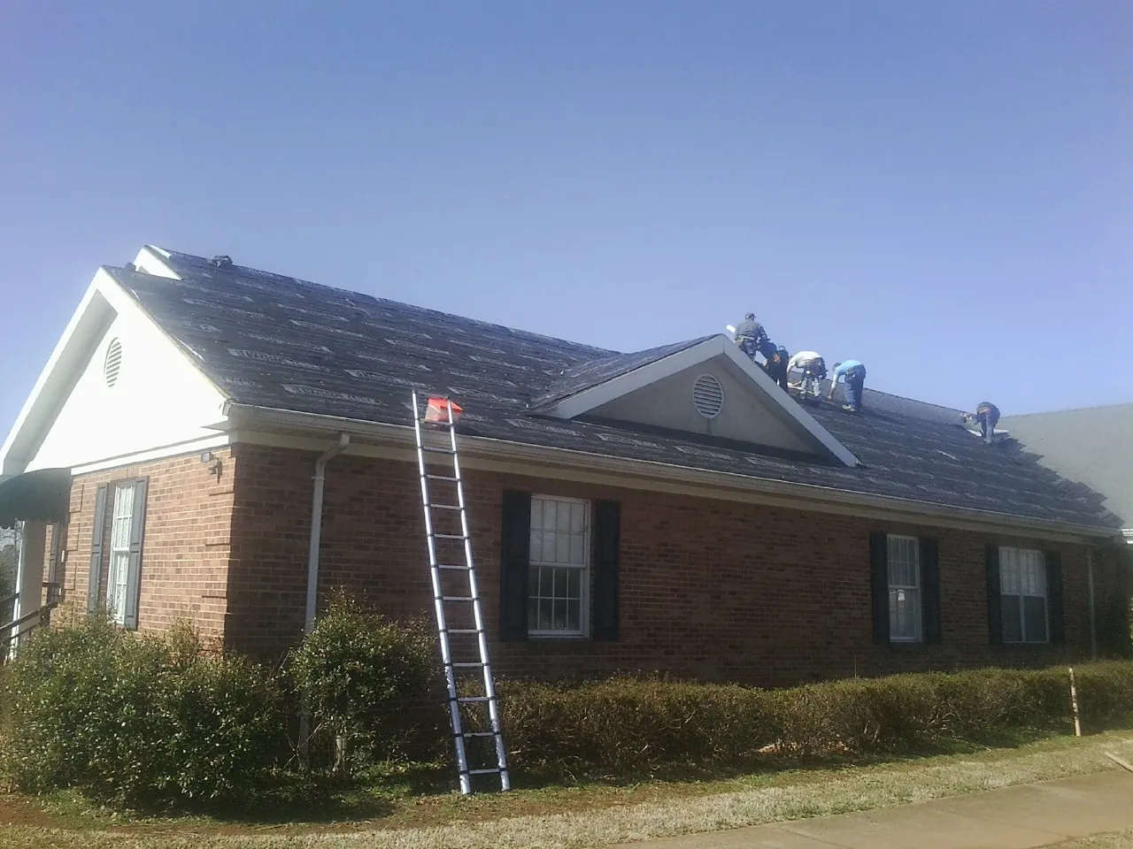 Crew tearing shingles off a brick ranch roof with a ladder set — Metal Roof Repair work by our crew in Clay City