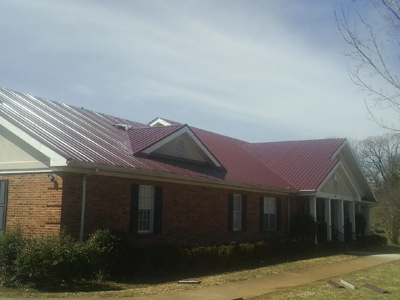 Red metal roof with gabled entries on a long brick building, from a Hail Damage Roof Repair job in Clay City