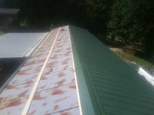 Old rusted panels beside newly installed green metal roofing — Wind Damage Roof Repair by Roofing Brothers in Clay City